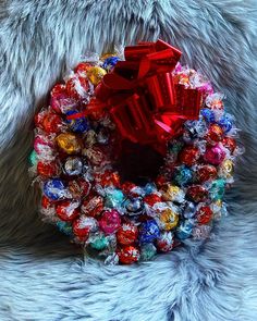 a wreath made out of candy and wrapped in red ribbon sitting on top of a furry surface