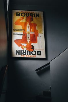 an old russian poster hangs on the wall next to a stair case in a dark room