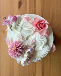 a white cake with pink flowers and swirls on it sitting on a wooden table