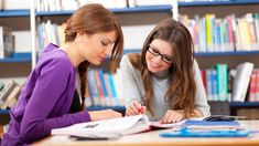 two young women sitting at a table in front of books and papers, one writing