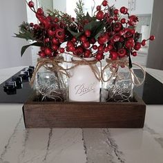 a vase filled with red berries and greenery on top of a wooden box next to a candle