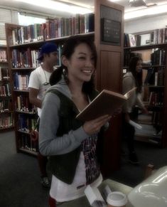 a woman standing in front of a bookshelf holding a book