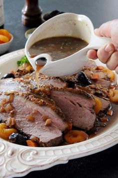 a person pours sauce on top of a plate of meat with vegetables and carrots