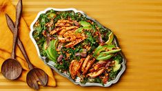 a salad with chicken, avocado and sesame seeds in a bowl next to two spoons