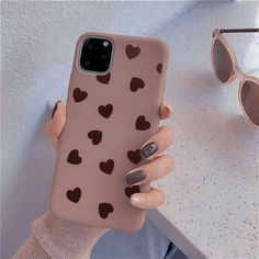 a woman's hand holding an iphone case with hearts on it and sunglasses next to her