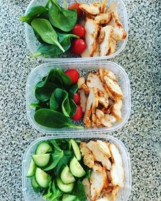 three plastic containers filled with chicken, spinach and cherry tomatoes on top of a table