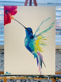 a painting of a hummingbird with a flower in it's beak on a easel