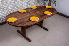 a wooden table with yellow plates on it in front of a brick wall and potted plant