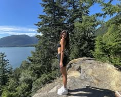 a woman standing on top of a rock next to trees and the ocean in the background