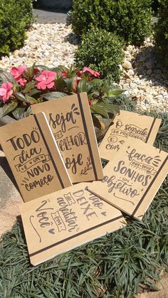 three brown paper signs sitting on top of green grass next to some bushes and flowers