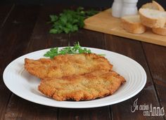 two fried fish fillets on a white plate with bread and parsley in the background