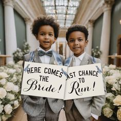 two young boys dressed in tuxedos holding signs that say here comes at chance the bride to run