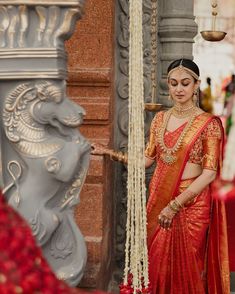 a woman in an orange and gold sari standing next to a pillar with beads hanging from it