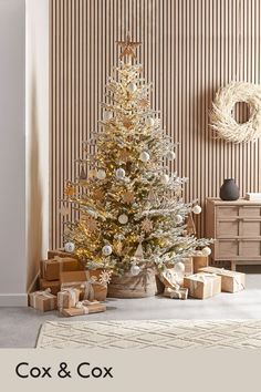 a white christmas tree surrounded by presents in front of a striped wallpapered room