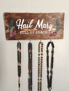 a sign that says hail mary full of grace hanging from a wall with several necklaces attached to it