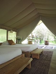 two beds in a large tent with wooden benches underneath the bed and an area rug on the floor