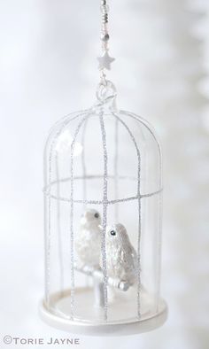 two white birds in a birdcage ornament hanging from a chain on a white background