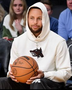 a man holding a basketball while wearing a hoodie and sitting in front of a crowd