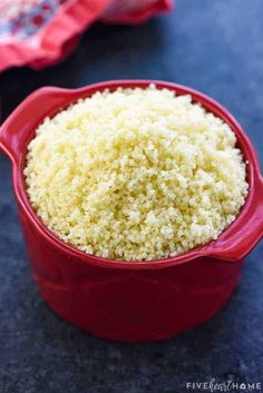 a red bowl filled with white rice on top of a table next to a napkin