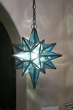 a blue glass star hanging from a chain in a room with white walls and flooring