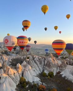 many hot air balloons are flying in the sky over some rocks and boulders at sunrise