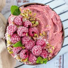 a bowl filled with raspberry smoothie topped with whipped cream and mint leaves