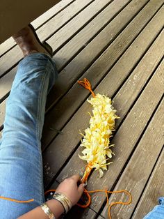 a person is sitting on a wooden bench with flowers in their lap and one hand holding an orange string