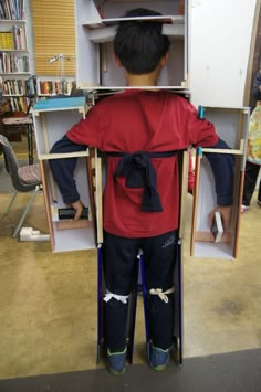 a young boy standing in front of a book shelf with his back to the camera