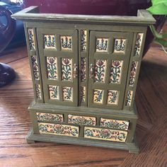 a green cabinet with flowers painted on the doors and drawers is sitting on a wooden table