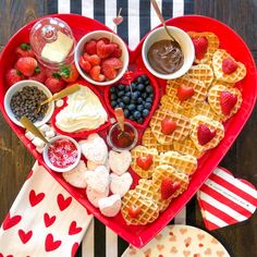 a heart shaped platter filled with waffles, fruit and dips on a table