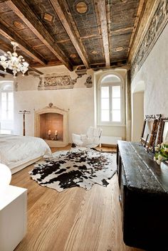 a bedroom with wood floors and white walls has a fireplace in the corner, along with a cow rug on the floor