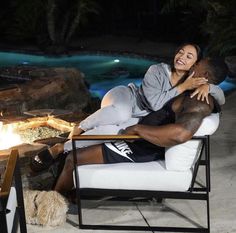 a man and woman sitting on a chair in front of a fire pit at night