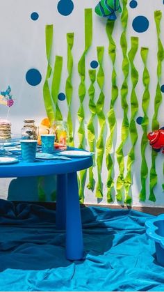 a blue table topped with cake next to a white wall covered in green streamers