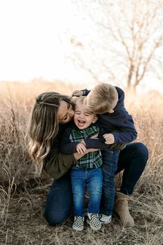 a mother and her two sons cuddle in the middle of a field with tall grass