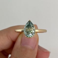 a person holding a yellow gold ring with an aquamarine colored stone in the middle