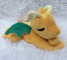 a yellow stuffed dragon laying on top of a fluffy white blanket with its eyes closed