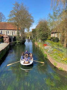 several people are in a small boat on the water near some houses and trees with flowers