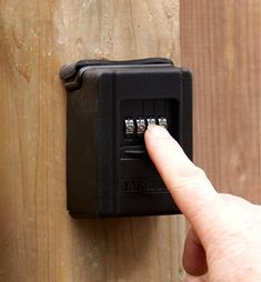 a hand is pressing the button on a wooden door lock that is attached to a wood fence