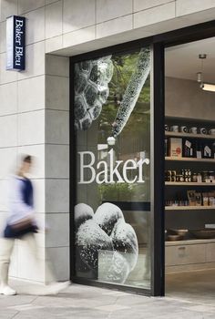 a man walking past a bakery shop window with the word baker on it's side