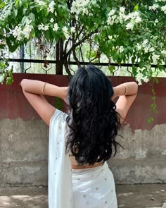 a woman with long black hair wearing a white sari and holding her hands behind her head