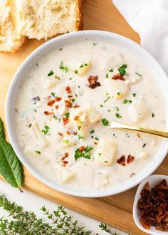 a white bowl filled with soup next to bread on a cutting board and spoons