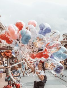 a woman is holding up many balloons in the shape of mickey and minnie mouses