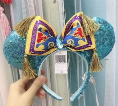 a hand holding up a mickey mouse ears headband with blue and yellow sequins