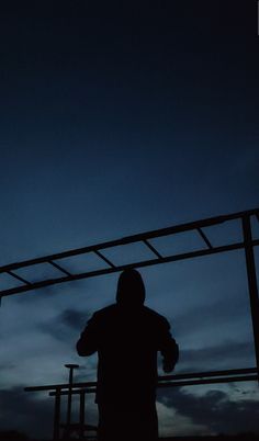 the silhouette of a person standing in front of a metal structure at night with their arms crossed