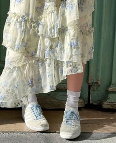 a woman wearing white shoes and a dress with blue flowers on it, standing in front of a green door