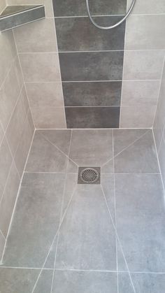 a shower with grey tiles and a drain in the floor next to it is shown