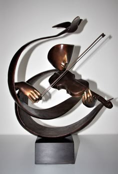 a metal sculpture that is on top of a wooden block and has a violin in it