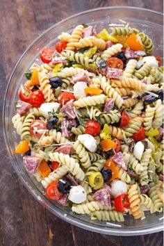 a pasta salad in a glass bowl on top of a wooden table