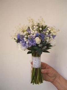 a person holding a bouquet of white and blue flowers in their left hand, against a white wall