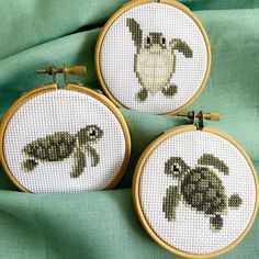 three cross - stitch turtle pictures are shown in two hoop frames on a green cloth